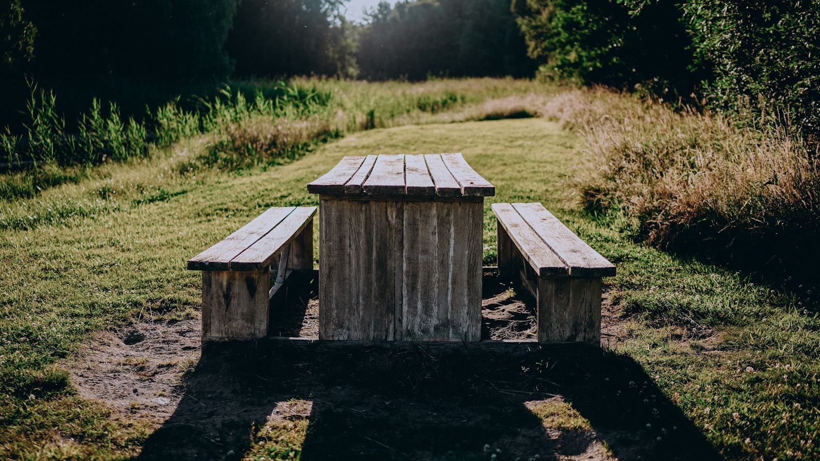 Una mesa larga de madera rústica con bancos, puesta al aire libre en un prado soleado