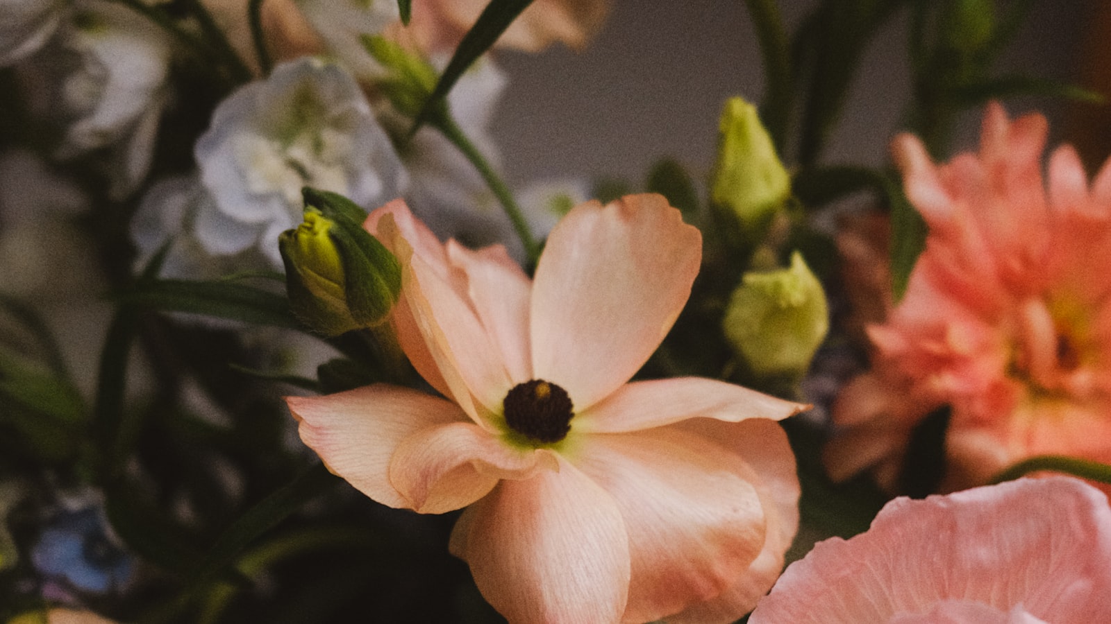 Primer plano de un ramo de flores en tonos rosa pálido, blanco y coral, con capullos verdes asomando entre los pétalos